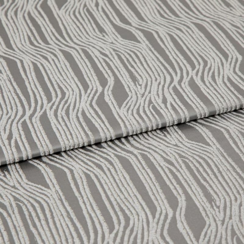 Textured grey upholstery fabric with raised white irregular vertical stripes, folded horizontally across the frame; fabric lies flat in a studio close-up with soft, diffuse lighting highlighting its sheen.