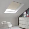 Room with white eaves wall, dark blue-grey wall to right with a shabby chic white drawer unit, a contemporary white chair, white painted floorboards and a skylight blind in cappucino.