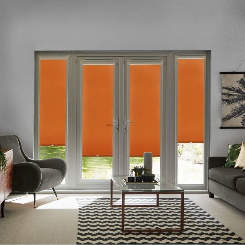 Orange roller blinds cover four-panel French doors and sidelights, lowered to conceal upper panes while revealing a garden strip; in a bright living room with grey sofas, glass coffee table.