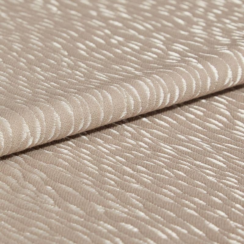 Beige jacquard fabric with glossy, raised crescent pattern; folded once across the frame, overlapping edges; close-up studio view with soft, diffuse lighting emphasizing the textured sheen.