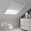 Room with white eaves wall, dark blue-grey wall to right with a shabby chic white drawer unit, a contemporary white chair, white painted floorboards and a skylight blind in pale grey.