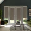 Floor-to-ceiling glass patio doors with beige roller blinds pulled down, framed by a dark wall; a glass coffee table on a black-and-white chevron rug sits between green armchairs, daylight outside.