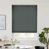 Dark gray pleated cellular shade lowered over a window, subtle vertical seams blocking most light while leaving a slim bright gap above a dining table with vase and potted plant.