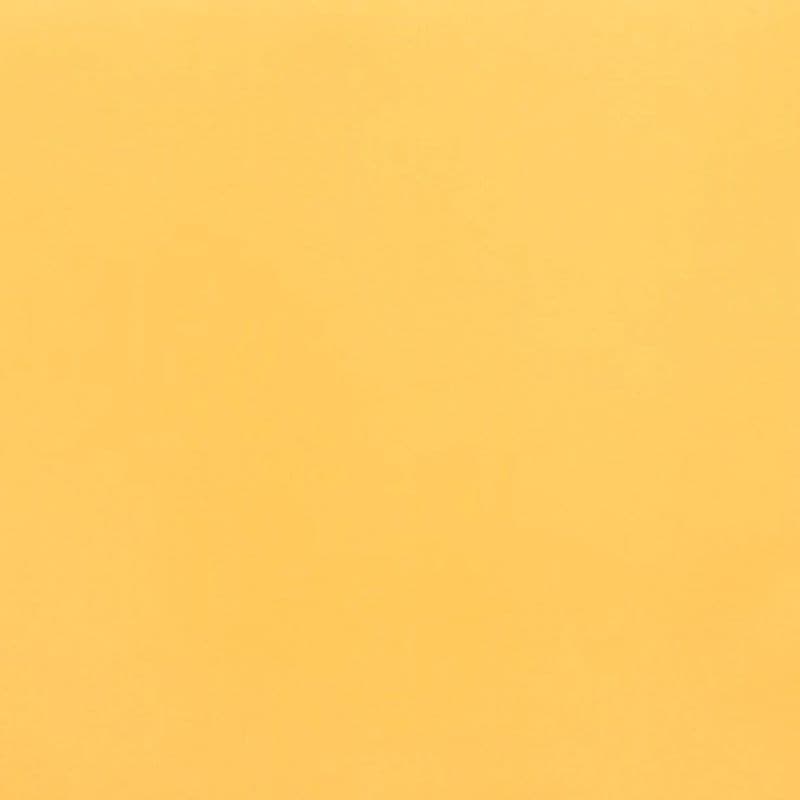 Ochre sheet of paper fills the frame (object), lying flat (action); soft, even lighting reveals slight texture in a uniform close-up field (context).