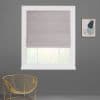 Light-grey fabric Roman shade lowered with a folded bottom, filtering daylight through a white-framed window; on a charcoal wall in a room with a gold wire chair and abstract art.