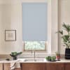 Light-blue roller blind covers most of a kitchen window, blocking light; stainless faucet and double sink sit beneath on a marble countertop, with bowls of greens, potted plants and a framed sketch nearby.