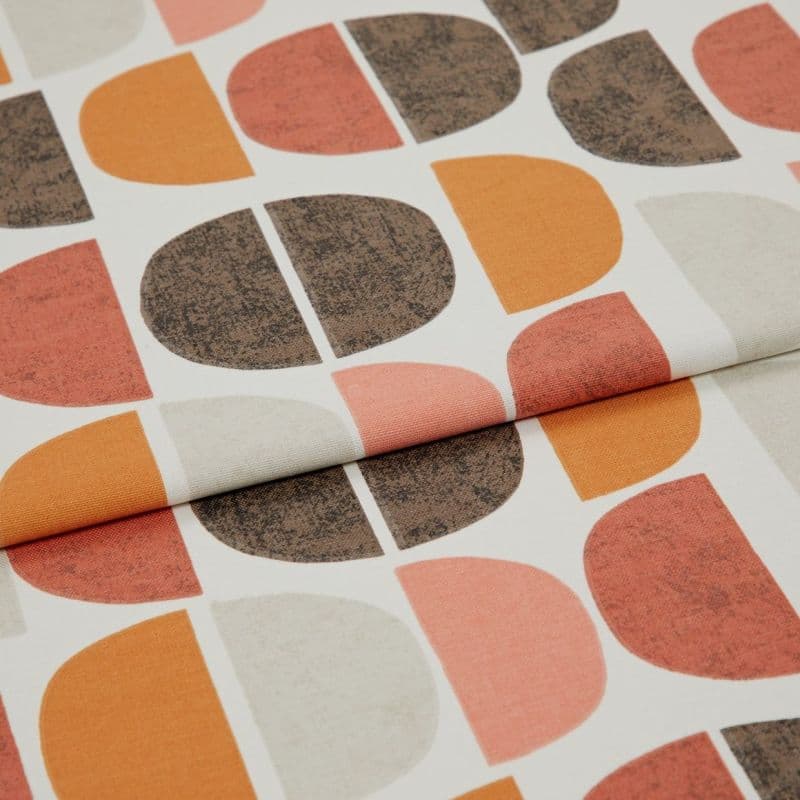 Printed fabric featuring repeated half‑circle motifs in orange, rust, beige and textured brown, folded once across the frame, photographed close-up on a neutral surface with soft, even lighting.