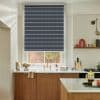 Navy horizontally striped roller blind lowered across the sash, filtering light and covering most of the window; kitchen with brass faucet, marble counters, wooden cabinets and a brick courtyard outside.