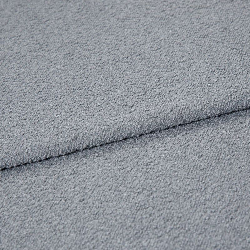Light-gray bouclé fabric folded once, showing pebbled loop texture; close-up macro view under soft, even lighting on a neutral surface, emphasizing tactile, cozy upholstery material.