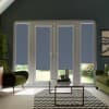 French glass doors with four narrow blue roller blinds lowered, blocking light while revealing a slim garden strip, set within a modern living room with green armchairs and a chevron rug.