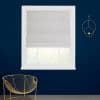 White patterned Roman shade lowered over a white-framed window, gently filtering daylight; set against a deep navy wall with a gold wire chair and circular gold wall sconce.