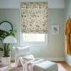 Printed Roman blind featuring cranes and blossoms, lowered over the window, filtering daylight into a pale-green reading nook with white lounge chair, potted plant, floor lamp and framed bird artwork.
