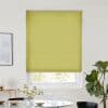 A lime-green pleated blind, fully lowered across a recessed window with vertical seams, blocking most light; modern dining area with white walls, table with glassware, flowers and a potted plant.