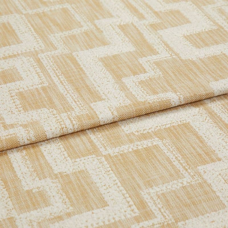 Curtain fabric folded and layered, woven beige cloth with raised cream geometric square/maze pattern; close-up textile shot on flat surface with soft, neutral lighting.