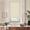Beige roller blind partially lowered over a window, filtering daylight; kitchen sink and faucet sit on marble countertop with plants, bowl of greens, framed sketch and wooden cabinets.