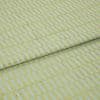 Textile fabric with raised yellow‑green rectangular grid pattern, folded once along a horizontal seam and overlapping, close-up studio-lit sample on a pale blue ground, showing textured weave.