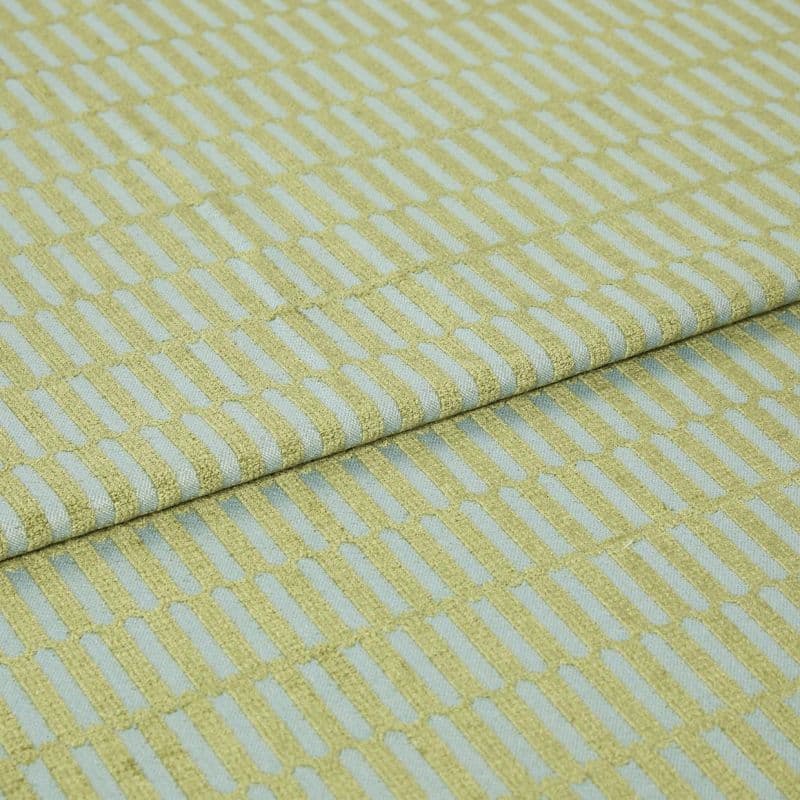 Textile fabric with raised yellow‑green rectangular grid pattern, folded once along a horizontal seam and overlapping, close-up studio-lit sample on a pale blue ground, showing textured weave.