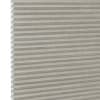 Honeycomb cellular fabric blind with horizontal pleats and textured beige finish, fully lowered and closed, diffusing soft light; set against a neutral, evenly lit wall with narrow white margin left.