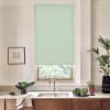 A pale green patterned roller blind covers and filters light through a kitchen window above a marble countertop with stainless sink and faucet, bowls of leafy greens and potted plants.