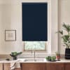 Window with a dark navy roller blind lowered above a stainless-steel sink and faucet, set in a minimalist kitchen countertop with potted plants, bowls of greens, and wood cabinets.