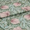 Folded woven fabric featuring a green botanical pattern of large pink flowers, pale blue-green leaves and small white blossoms, folded across the frame, showing textured weave under soft even lighting.