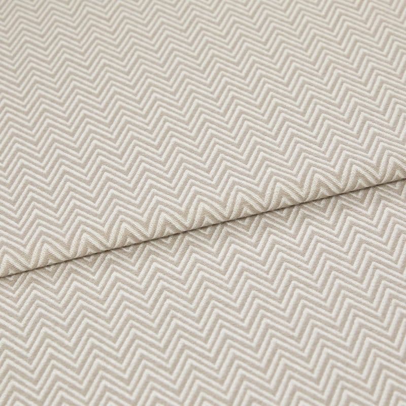 Beige chevron-embossed fabric folded diagonally, showing repeated raised zigzag pattern; close-up, evenly lit textile surface emphasizing texture and subtle two-tone threads.