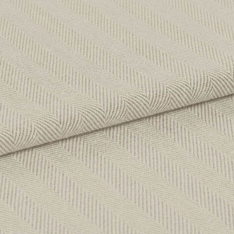 Cream herringbone-woven fabric folded diagonally, showing raised ribbed chevron pattern; laid flat under soft, even lighting for a close-up textile detail.