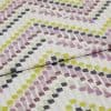 Folded cotton fabric with painterly square brushstrokes (mauve, chartreuse, olive, charcoal) arranged in staggered rows — folded across the frame, close-up on a flat surface under soft, diffuse lighting.