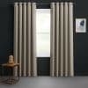 Beige grommet-top curtains, floor-length and pleated, hang on a metal rod, slightly parted to admit diffused daylight; dark charcoal-walled room with a wooden side table, glass-cloche lamp, abstract art.