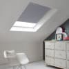Room with white eaves wall, dark blue-grey wall to right with a shabby chic white drawer unit, a contemporary white chair, white painted floorboards and a skylight blind in pale charcoal grey.