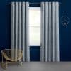 Grey grommet-top curtains, hanging in pleats on a rod and parted to reveal a bright window, against a deep navy wall with a gold chair and round wall decor.