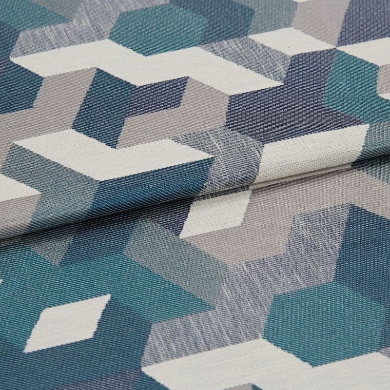 Woven upholstery fabric with teal, navy, gray and white isometric geometric pattern — folded once, overlapping — close-up on a flat surface under soft, neutral lighting.