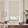 Beige roller blind is lowered over a window, filtering daylight above a kitchen sink with stainless faucet, countertop bowl of leafy greens, potted plants, and a framed architectural sketch.