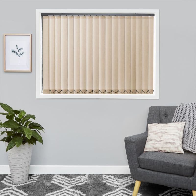 Beige vertical blinds, evenly spaced slats with bottom bead chain, fully closed over a white-framed window, softly filtering daylight in a gray living room with armchair, plant, framed botanical print.