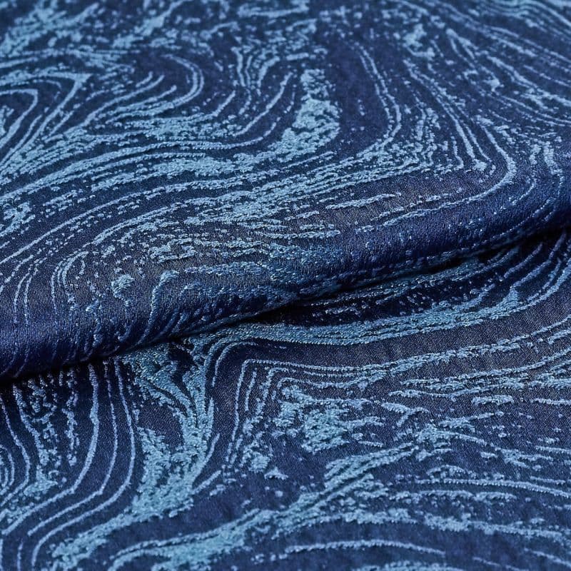 Dark navy jacquard fabric with raised, tufted wavy pattern folded over itself, revealing woodgrain-like texture; close-up studio shot with soft lighting accentuating sheen and depth.