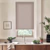 Patterned roller blind covers window above a stainless faucet, partially blocking daylight; kitchen countertop below holds a sink, a bowl of leafy vegetables, small potted plants and framed art.