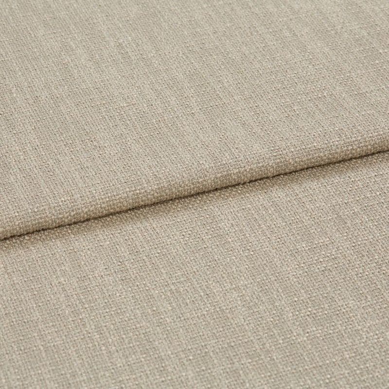 Beige woven fabric folded into overlapping panels, showing coarse textured upholstery weave; a horizontal fold/edge across frame, close-up studio-lit view suggesting a sofa cushion or fabric sample.