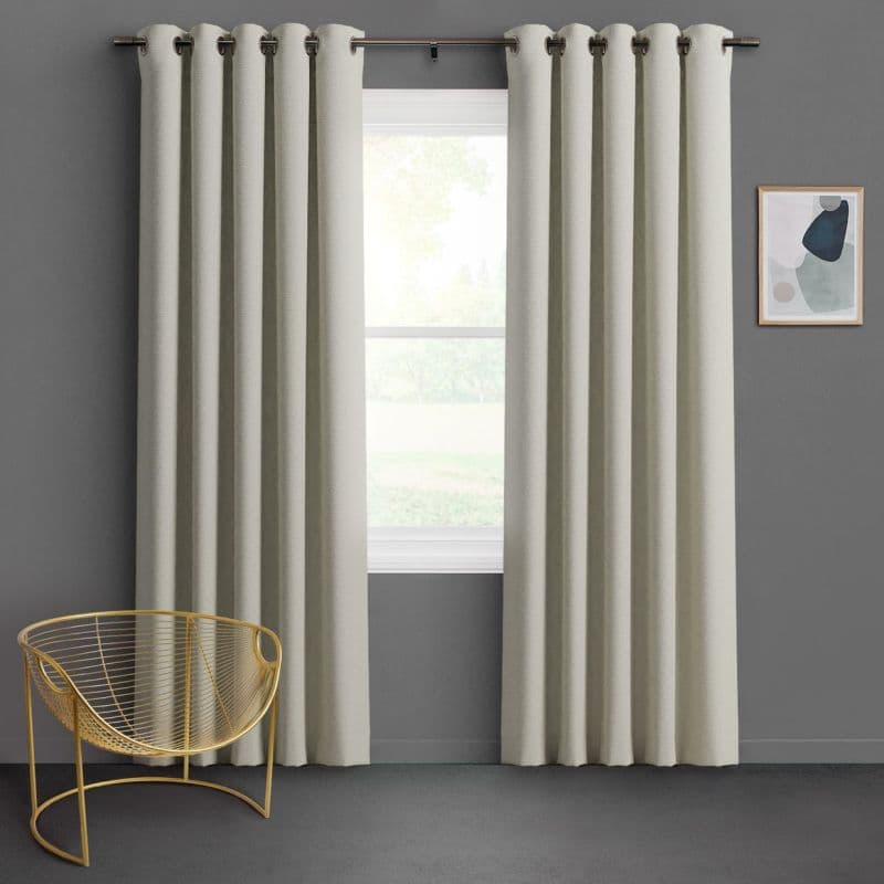 Textured beige grommet-top curtains hang on a metal rod, parted to frame and softly filter daylight through a centered window; gray-walled room with a gold wire chair and abstract art.