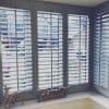 White wooden plantation shutters cover a three-panel bay window, slats tilted open to filter bright daylight and show a suburban street; windowsill holds a wooden "Family" sign and deer ornament.
Transcription:
Family
WHERE LIFE BEGINS & LOVE NEVER ENDS