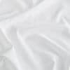 White satin fabric spread across a surface, rumpled into gentle folds and creases that catch soft diffuse light, close-up view with a neutral background.