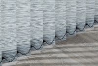 Vertical fabric blinds: light-gray slats with horizontal black stripes and a scalloped black bead motif along lower edges — hanging closed — filtering daylight, casting shadows on a light wood floor.
