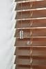 Wooden horizontal venetian blinds with brown wood-grain slats and pull cords bearing a chrome weight; partially closed, slightly angled to filter light in a close-up against a white wall.
