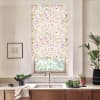 Floral-patterned Roman blind covers a kitchen window; it hangs above a sink and faucet, amid a countertop with bowls of vegetables, potted plants, and a framed sketch.