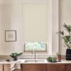 Beige roller blind hangs lowered over a kitchen window above a stainless sink and faucet; marble countertop holds a bowl of greens, potted plants and a framed sketch.