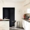 Black horizontal venetian blinds cover a sliding glass door, fully closed and dimming light. In a contemporary white kitchen with island, chrome bar stool, stainless bin, sunburst clock and tulips.