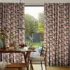 Full-length pleated patterned curtains (semi-circle design, orange, pink, brown) drawn to sides, framing a central opening that lets soft daylight through; dining table and pendant light face a green backyard.