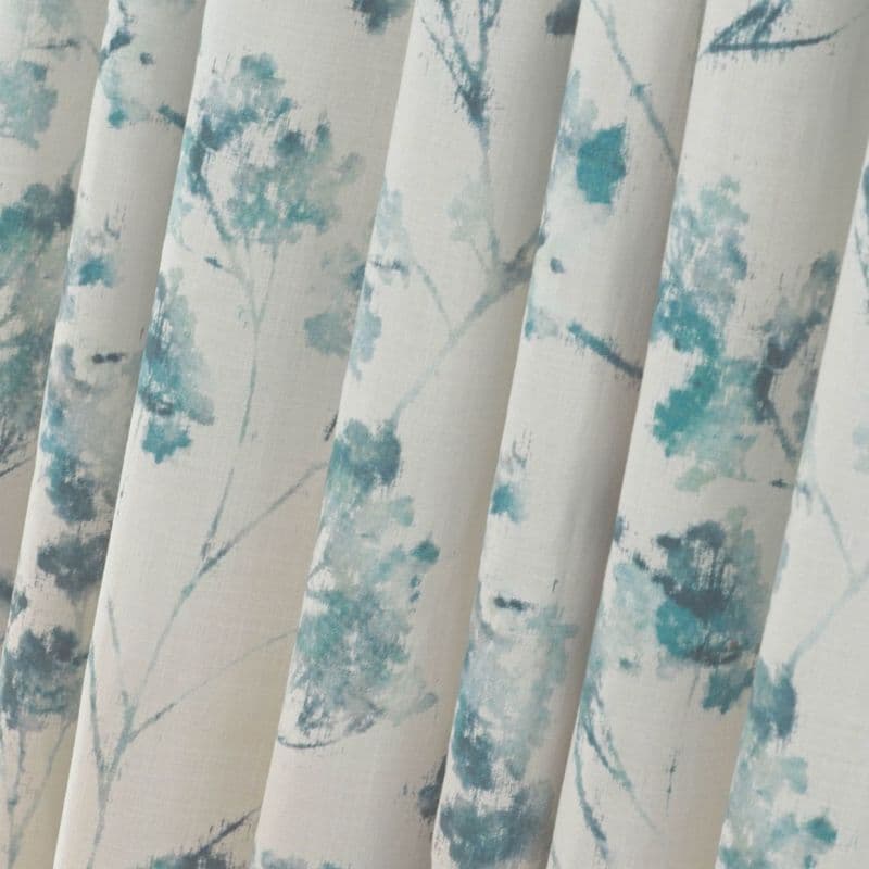 Fabric curtains with vertical pleats and teal watercolor floral print, hanging in soft folds; close-up interior view with neutral cream background and diffuse natural light.