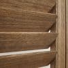 Louvered wooden shutters with wide horizontal slats, angled slightly open, showing pronounced wood grain and beveled edges, close-up interior view with warm tones and light through narrow gaps.