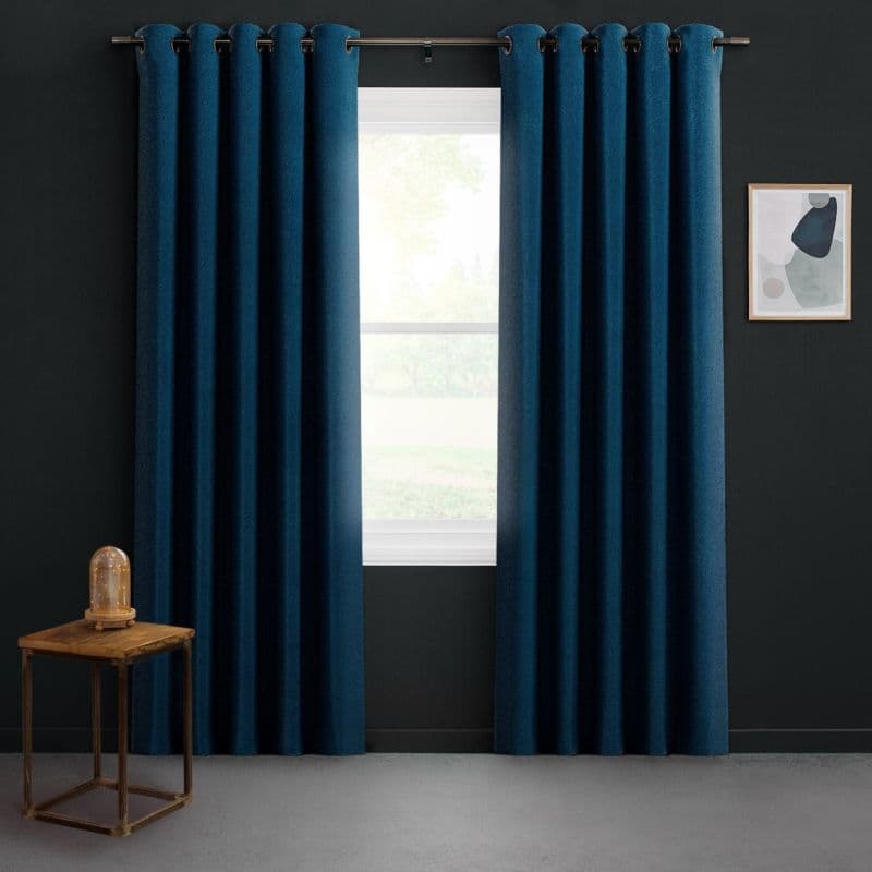 Floor-length navy grommet curtains on a metal rod, parted to reveal bright daylight through a white-framed window; dark-gray room with a small wooden side table and framed abstract art.