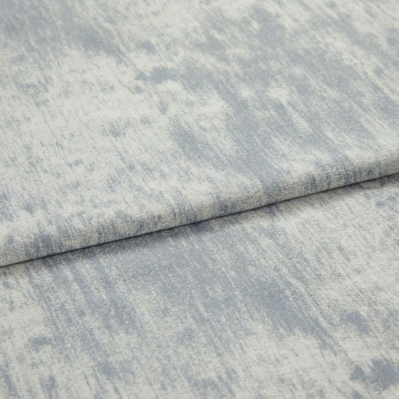 Folded textured fabric with pale blue-gray, mottled brushed pattern; fabric layered in a horizontal fold, lying flat under soft, even studio lighting in a close-up view.